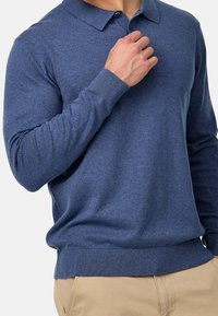 Granatowa, długosleeve polo z kołnierzykiem, ściągaczami u rękawów i prostym dołem. Wykonana z miękkiej, teksturowanej tkaniny, z zapięciem na guziki.