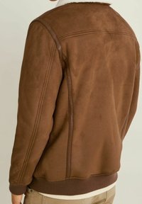 Uomo che indossa una giacca in suede marrone con polsini e orlo a coste, caratterizzata da un colletto in pelliccia shearling bianca, mostrato di spalle.