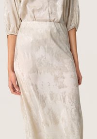 Satin, cremefarvet nederdel med en subtil metallisk glans og et abstrakt lys gråt mønster. Elastisk talje og let flydende design.