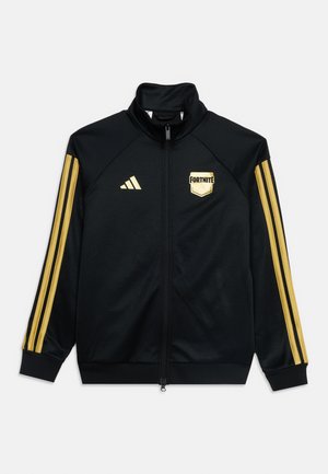 Μαύρο τζάκετ με φερμουάρ και χρυσές ρίγες Adidas στα μανίκια, χρυσλό λογότυπο Adidas στο δεξί στήθος και χρυσλό έμβλημα Fortnite στο αριστερό στήθος.