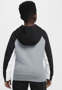 Sudadera con capucha negra y gris con acentos blancos, que presenta una cremallera y puños acanalados. La textura de la tela es suave. Vista desde la parte posterior.