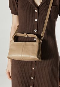 Bež torba od kože s teksturiranim završetkom, kratkom drškom i odvojivim remenom. Mala veličina, pravokutnog oblika, s suptilnim detaljem šava.