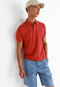 Punane polo särk mugava lõikega, lühikeste varrukatega ja nööbiplikaat, kombineeritud helesiniste teksashortsidega, millel on plaattaskud.