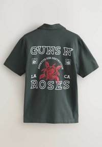 Tmavě zelené bavlněné polo triko s velkým grafickým motivem červené růže a bílým textem, který zní "GUNS N' ROSES" a "APPETITE FOR DESTRUCTION."