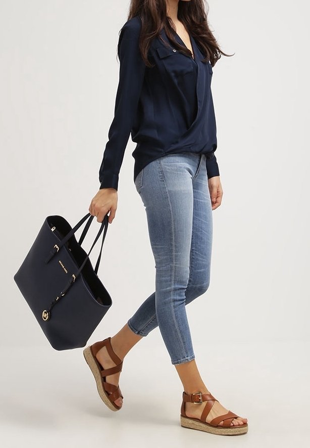 Marineblauwe draagtas met dubbele handgrepen, gecombineerd met een donkerblouse, lichtblauwe spijkerbroek en bruine sandaal met sleehak en bandjes.