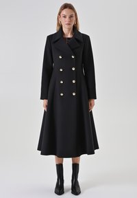 Doppelseitiger schwarzer Mantel mit großen goldenen Knöpfen, weitem Kragen und langen Ärmeln. Glockenförmiges Design reicht bis zur Mitte der Wade. Glatte Textur.