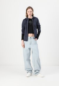 Marineblå zip-up hettegenser med logo, svart cropped topp, lyseblå høytlivs vide jeans og hvite joggesko. Glatte stoffteksturer.