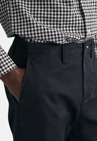 Sort-hvid ternet skjorte med klassisk krave, parret med marineblå chinos. Chinos har sidelommer og en frontknaplukning.