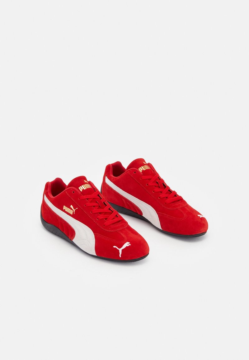 Paire de baskets rouges Puma avec des bandes blanches sur les côtés, des semelles noires et des logos Puma dorés sur fond blanc.