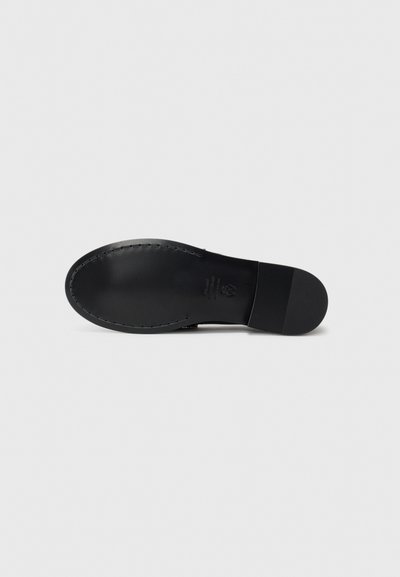 Semelle de chaussure en cuir noir avec une texture lisse, une forme arrondie et des coutures visibles le long du bord. Design minimaliste sans décorations notables.