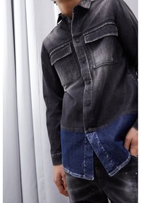 Camicia in denim nera e blu con due tasche sul petto e bottoni, caratterizzata da un design a gradiente che passa da un blu scuro a uno più chiaro verso l'orlo.