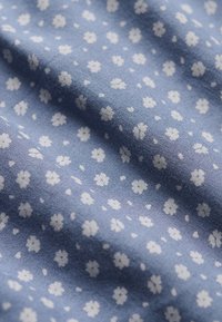 Tissu bleu clair avec de petits motifs floraux blancs dispersés et de doux plis créant des ombres délicates et de la texture.