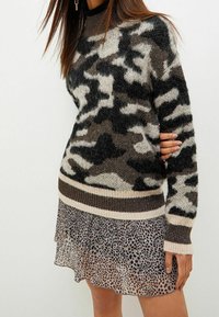 Maglione a motivo camouflage in nero, beige e grigio con una finitura testurizzata; abbinato a una gonna a strati trasparente con stampa leopardata.