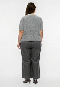 Maglione grigio a maniche corte con una finitura testurizzata e un colletto decorato con perle, abbinato a pantaloni larghi a righe grigie e tacchi lucidi.