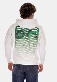 Felpa bianca con un design di un serpente verde sulla schiena, caratterizzata da un motivo a rete sfumata. Il tessuto appare morbido, con una vestibilità rilassata e cappuccio regolabile.