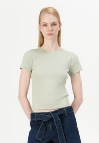 Light green, fitted short-sleeve t-shirt with a ribbed texture and crew neck. Paired with high-waisted dark denim pants featuring a tied belt.