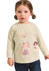 Svetlozelená košeľa s dlhým rukávom, zdobená hravými ilustrovanými postavičkami, kvetinovými vzormi a jemnou textúrou; doplnená tmavomodrými džínami.