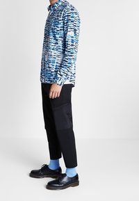 Camicia a maniche lunghe con motivo astratto blu, abbinata a pantaloni neri, calzini blu e scarpe stringate nere.