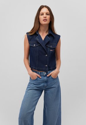 Dark blue denim sleeveless jacket featuring a collar, front buttons, and two chest pockets. Paired with light blue wide-leg jeans.
