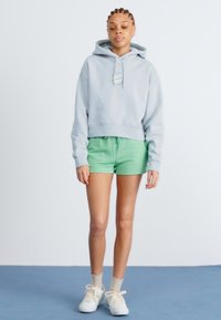 Light gray cropped hoodie with a logo, paired with green shorts. The outfit is complemented by white sneakers and beige socks.