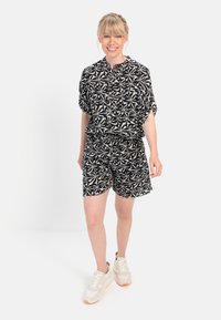 Sort-hvid mønstret kortærmet skjorte og matchende shorts, med elastisk talje og afslappet pasform. Styles med lyse sneakers.