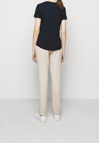 Marinblå bomullströja med korta ärmar, rundad nederkant, i kombination med beige skräddarsydda byxor och vita sneakers, med släta texturer.