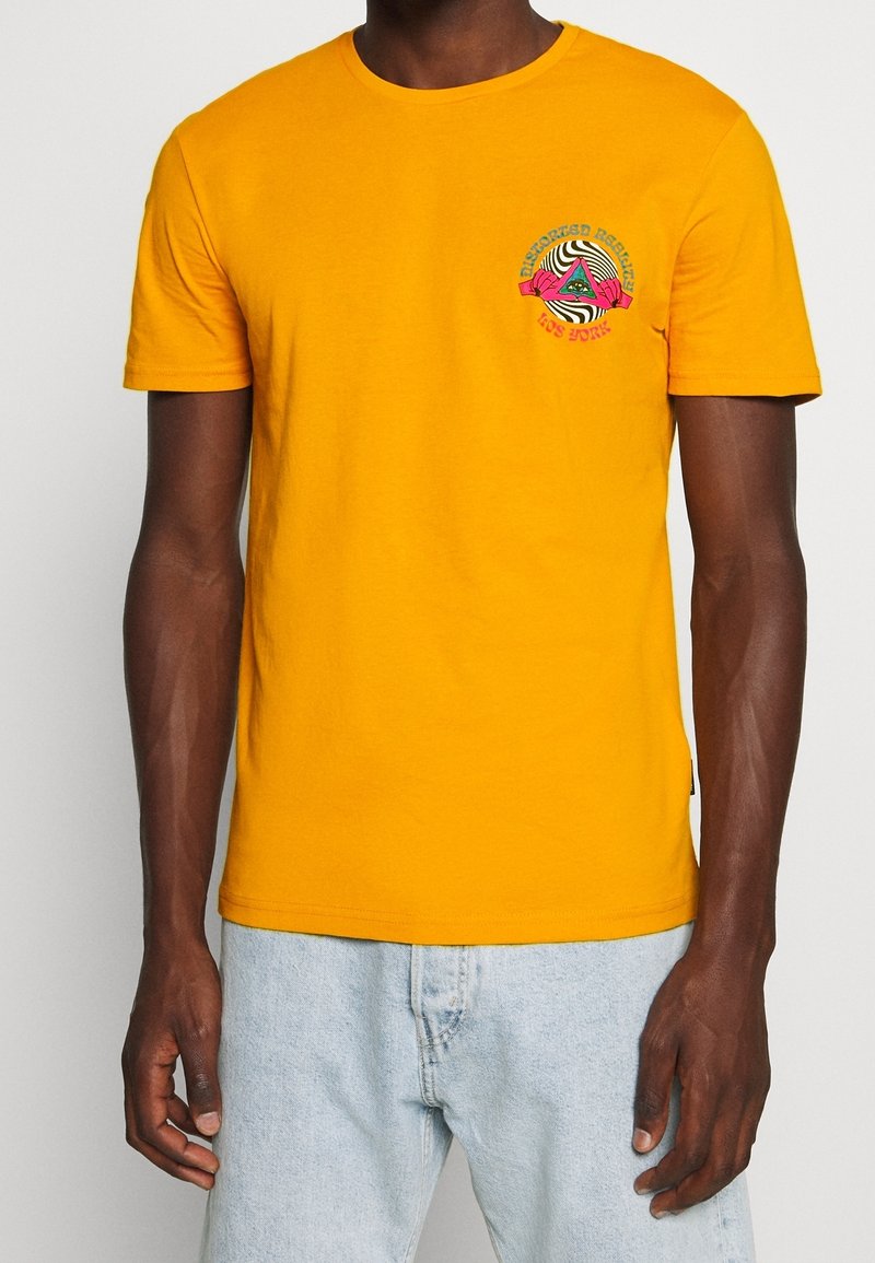 Hořčičně žluté bavlněné tričko s krátkými rukávy, s kruhovým grafickým designem v zelené, růžové a červené barvě na levé straně hrudi.