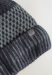 Knit beanie in dark gray and light gray, featuring a textured pattern with a cuffed hem and a small textured logo patch.
