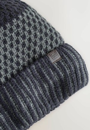 Knit beanie in dark gray and light gray, featuring a textured pattern with a cuffed hem and a small textured logo patch.