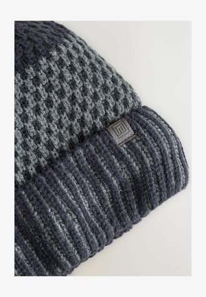 Knit beanie in dark gray and light gray, featuring a textured pattern with a cuffed hem and a small textured logo patch.