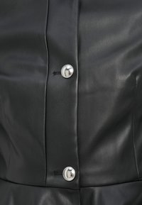 Μαύρο δερμάτινο ένδυμα με ασημένια κουμπιά, λεία υφή και εφαρμοστή σχεδίαση με κεντρική ραφή.