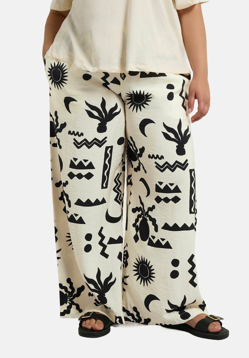 Pantalons larges en tissu crème avec des motifs abstraits noirs, incluant des soleils, des zigzags et des silhouettes. Fabriqués à partir d'un matériau doux et texturé.