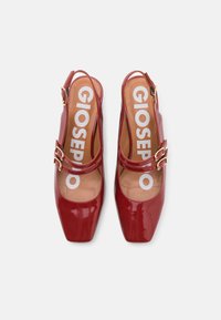 Chaussures slingback en cuir verni rouge avec un bout carré, ornées de deux boucles métalliques et d'une semelle intérieure rembourrée.