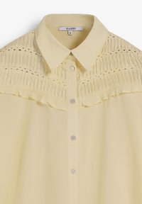 Chemise jaune à manches longues avec col, présentant un smocké texturé aux épaules et un corps lisse. Comprend des boutons en plastique.