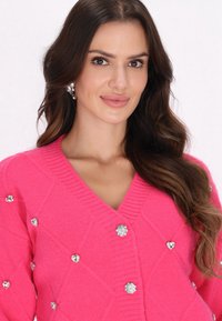 Cardigan roz cu decolteu în V, având o textură în model diamant și embellishments din strasuri rotunde și în formă de inimă.