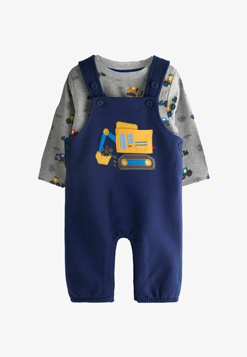 Bērnu apģērbs ar tumši ziliem kombinezoniem, uz kuriem ir dzeltena ekskavatora aplikācija, valkāts virs pelēkas, garām piedurknēm krekla ar transportlīdzekļu apdruku.