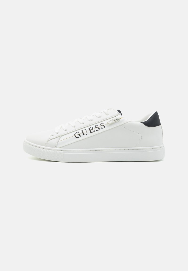 Vit sneaker med slät syntetläderöverdel, snörningsdesign, svart hälaccent och "GUESS"-logotyp på sidan. Mönstrad gummisula.
