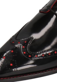 Sort laklæder sko med spids tå, perforerede detaljer og røde accenter langs kanten og hulmønstrene.