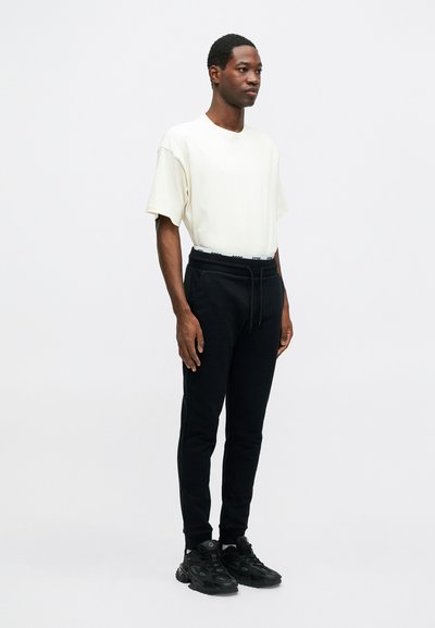 Cream short-sleeve t-shirt paired with black joggers featuring a drawstring and elastic waistband, completed with black athletic sneakers.