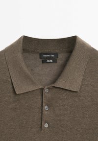 Hnědá lněná polo košile s texturovaným povrchem, která má klasický límec, tříknoflíkovou légu a štítek s nápisem "Massimo Dutti."
