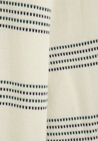 Pull en tricot avec une base crème, présentant des rayures horizontales de petits pois vert foncé et bleu marine. Texture douce et design classique.