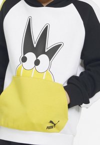 Bluza z kapturem z czarnymi rękawami i białym korpusem. Posiada żółtą kieszeń z rysunkową twarzą oraz czarnym logo Puma na dolnym brzegu.