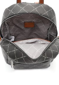 Musta kuvioitu reppu, jonka pääsäiliö on avoinna ja näyttää harmaan vuorin sekä sisäpuolella olevan pienen vetoketjullisen taskun.