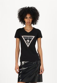 T-shirt in cotone nero con scollo a V, caratterizzato da un design a triangolo in rosa e bianco, impreziosito da strass. Abbinato a una gonna in vinile nera.