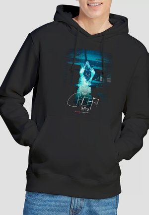 Person wearing black hoodie with graphic of a ghostly figure holding a rope and text "The Creep Tapes" on the front.