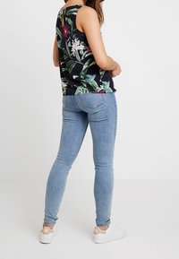 Top senza maniche a stampa floreale nera con foglie verdi e dettagli rosa, abbinato a jeans skinny azzurri chiari e sneakers bianche.
