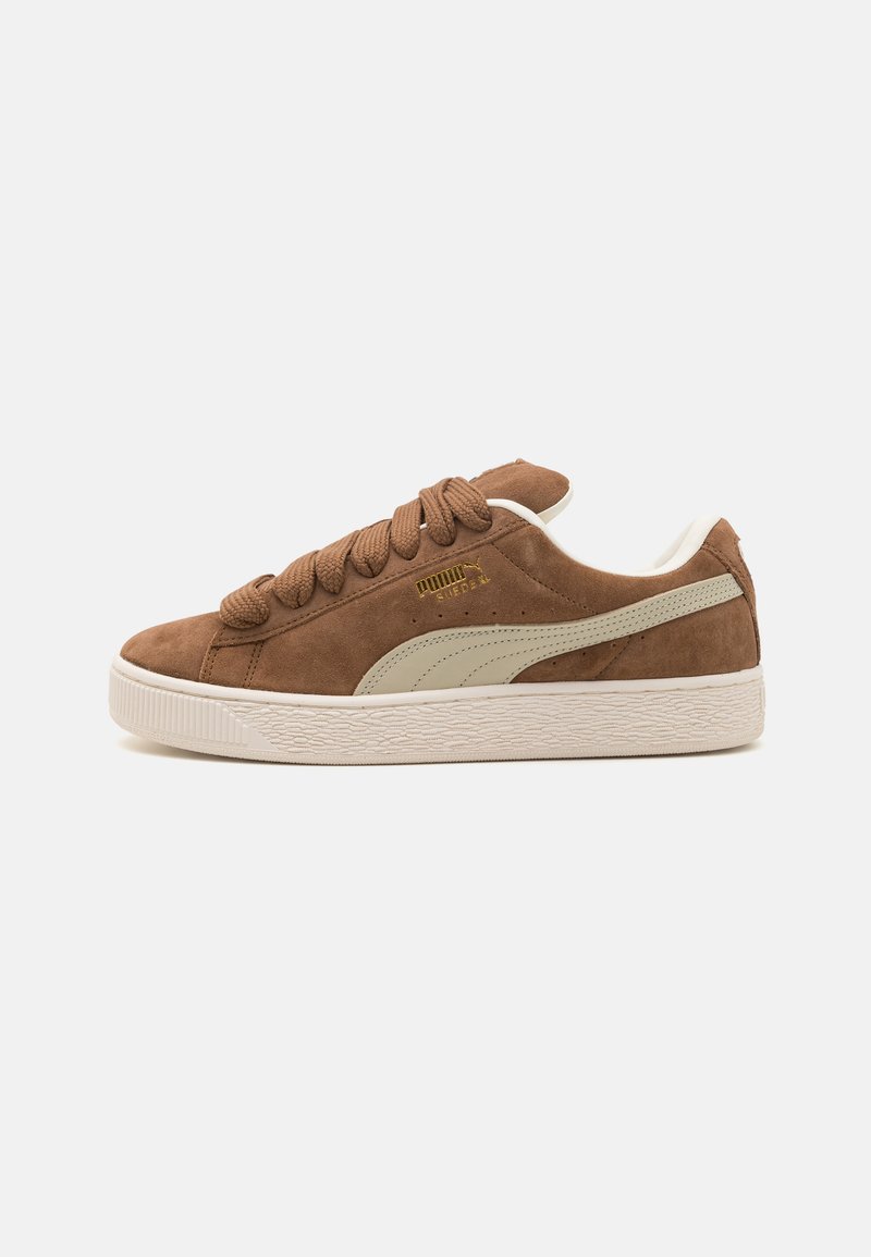 Brown suede sneaker with cream accents, flat laces, textured white rubber sole, and gold logo detail on the side. Classic low-top design.
