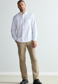White button-down shirt with pocket, beige pants, and black shoes. The shirt has a smooth texture; the pants are straight-leg.