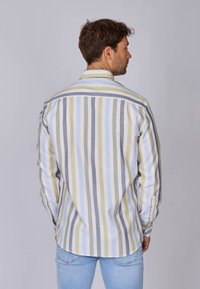 Chemise à rayures à manches longues en coton blanc, jaune, bleu clair et gris. Présente un empiècement arrière incliné et des poignets à boutons, avec un ourlet arrondi.
