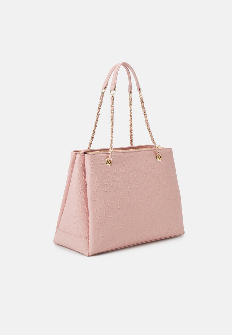 Sac fourre-tout rose avec logo en relief, forme structurée, texture lisse, poignées à double chaîne et accents en ton doré. Fermeture zippée en haut.